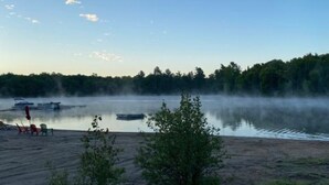 A lakeside view with a dock, chairs, and a small boat. - Site #45 | Blue Lake Bunkie (Whitestone)