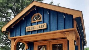 A wooden cabin with a blue exterior and a sign reading "BLUE LAKE". - Site #45 | Blue Lake Bunkie (Whitestone)
