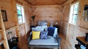 A cozy wooden cabin room with a bed, a small table, and a chair. - Site #45 | Blue Lake Bunkie (Whitestone)