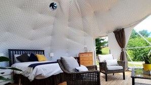 Ein Schlafzimmer mit Bett, Kommode und Sitzecke mit Blick auf Grünfläche.