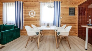 A wooden cabin interior with a dining table, four chairs, a green sofa, and a ship's wheel decoration. - Nice apartment in Jaroslawiec with WiFi (Jaroslawiec)
