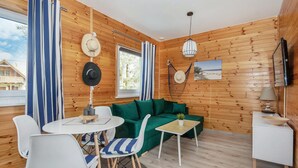 A cozy cabin interior with a green sofa, white chairs, a small round table, and wooden walls. - Nice apartment in Jaroslawiec with WiFi (Jaroslawiec)