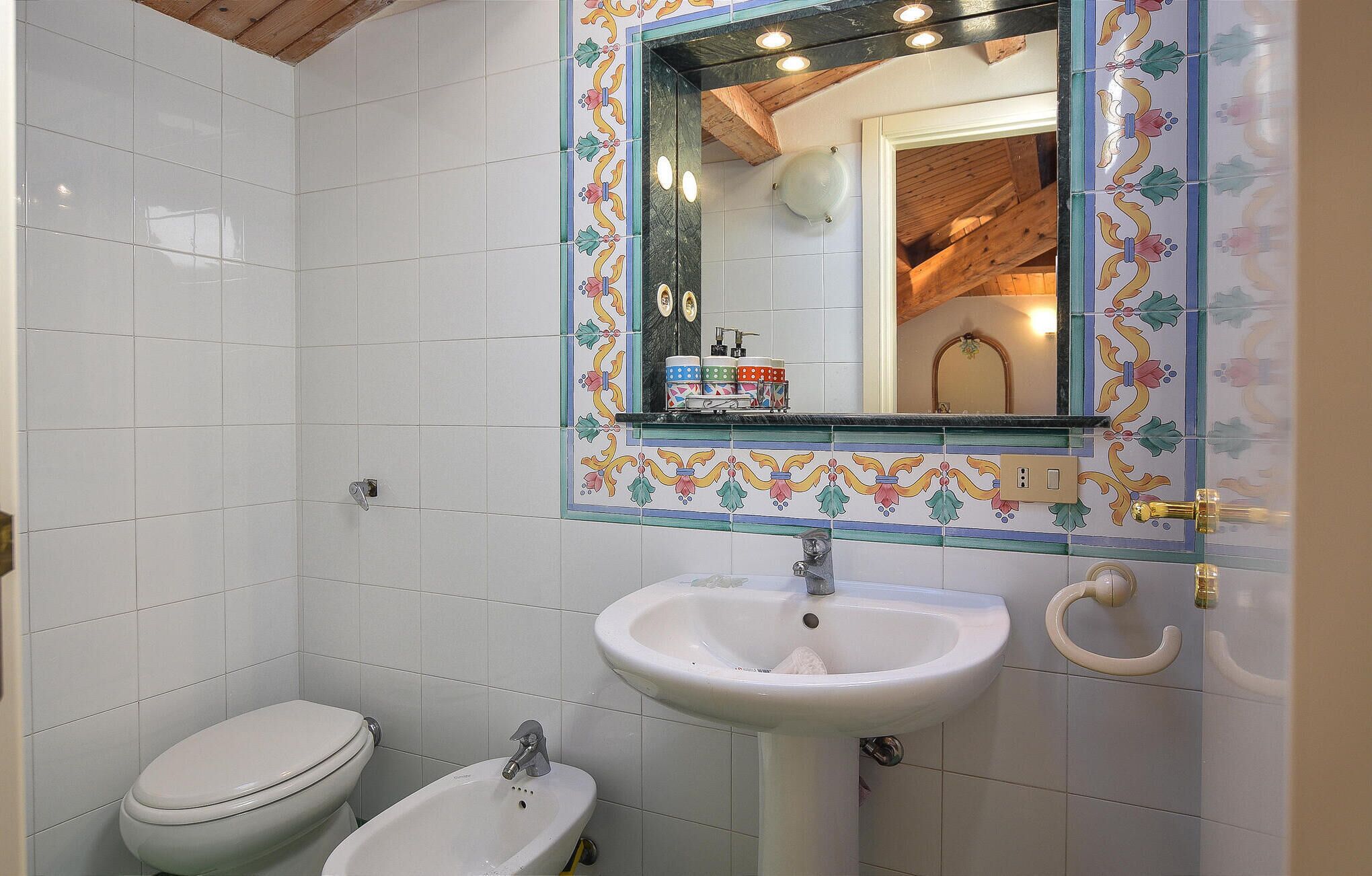 Een badkamer met witte tegels, een wit wastafel, een bidet en een spiegel met een bloemenrand.