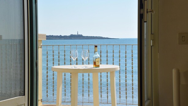 A balcony with a table set for two, a bottle of wine, and two wine glasses. - Cozy home in Sampieri with WiFi (Sampieri)