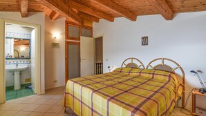 A bedroom with a wooden ceiling, a bed with a plaid bedspread, a bedside table with a lamp, and a bathroom visible through an open door. - Cozy home in Sampieri with WiFi (Sampieri)