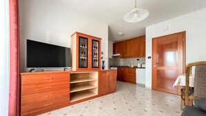 A modern living room with a TV, wooden cabinets, a dining area, and a kitchen.