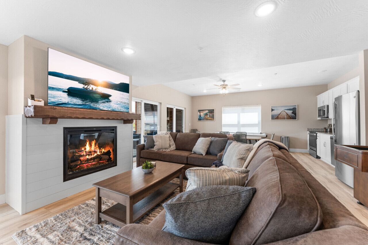 A modern living room with a fireplace, a large flat-screen TV, a sofa, and a kitchen area in the background.