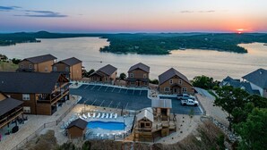 Un complexe hôtelier au bord d’un lac, comprenant plusieurs chalets en bois, une piscine et un parking.