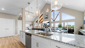 Una cocina amplia con encimeras de granito, armarios blancos e iluminación colgante.
