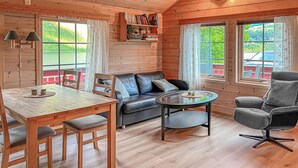 Interior acollidor d'una cabana amb una taula de dinar de fusta, un sofà de cuir, una taula de cafè rodona i un butaca grisa.