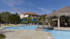 A pool area with lounge chairs, umbrellas, and a thatched-roof structure. - Peaceful Studio in Ocean Dream (Cabarete)