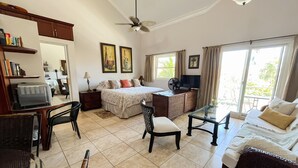 A well-lit room with a bed, a desk, a chair, a television, and a ceiling fan. - Peaceful Studio in Ocean Dream (Cabarete)
