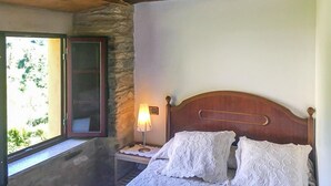 Quarto com cabeceira de madeira, luminária de cabeceira e janela com vista para vegetação.