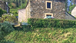Um edifício de pedra com uma pequena janela e porta, cercado por vegetação e um viveiro.