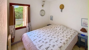 A bedroom with a bed, a window, a wall clock, and a small table with a lamp.