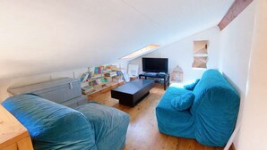 A loft-style living room with a wooden floor, a black entertainment unit, a blue sofa, and a bookshelf.