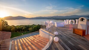 Eine Dachterrasse mit Holzdeck, weißen Möbeln und Blick auf einen See und Berge.