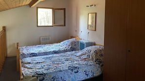 A bedroom with a wooden ceiling, a bed with floral bedding, a bedside table, a mirror, and a wardrobe.