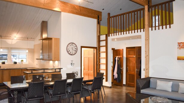 A spacious living area with a dining table and chairs, a sofa, and a staircase leading to an upper level.