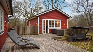 A red wooden cabin with a deck, a covered seating area, and a wooden fence.