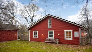 A red wooden house with a bench in front, surrounded by trees and a grassy yard.