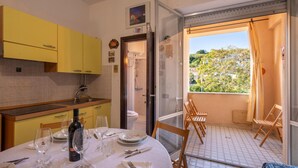 A kitchen with yellow cabinets, a dining table set for four, and a glass-enclosed balcony with a view of greenery. - Lovely apartment in Ortona with WiFi (Ortona)