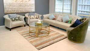 Una sala de estar con un sofá, sillones, una mesa de centro de vidrio y un sillón verde.