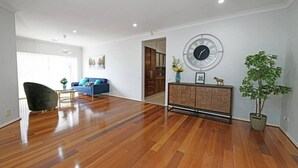 Un salón espacioso con suelo de madera, un sofá azul, un sillón negro, un reloj de pared redondo y una planta en maceta.