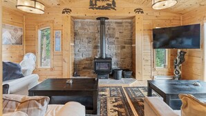 A wooden cabin interior with a stone fireplace, a television, and a cozy seating area.