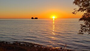 Um pôr do sol sobre um mar calmo, com uma costa rochosa e uma terra à distância.
