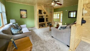 Uma sala de estar aconchegante com dois sofás, um rack de madeira e um ventilador de teto.