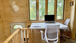 Interior de cabana com escrivaninha, computador, cadeira de escritório e cabeça de veado montada.