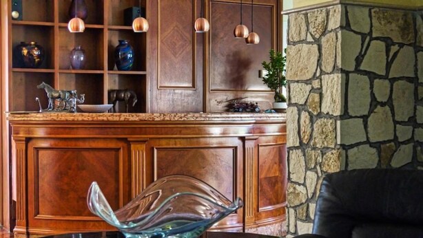 Una zona de bar con barra de madera, un jarrón de cristal como centro de mesa, lámparas colgantes de cobre y una pared de piedra.