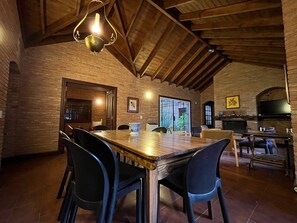 A rustic dining area with a wooden table and chairs, a hanging light fixture, and a brick wall.