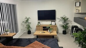 A modern living room with a sofa, a coffee table, a TV, and potted plants. - Our Townhouse in Toowoomba (Newtown)