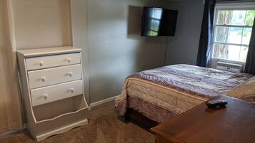 Un dormitorio con cama, cómoda, televisor montado en la pared y ventana con cortinas.