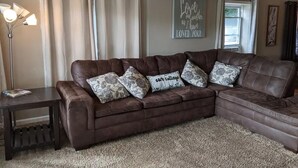 A living room with a brown leather sectional sofa, a small table, and a floor lamp. - Riverfront Cottage with Hot Tub, Kayaks, Canoes, & Fishing Boats! (Waterville)