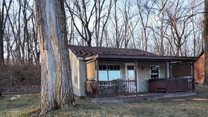 A small, single-story building with a porch and a fenced yard. - Riverfront Cottage with Hot Tub, Kayaks, Canoes, & Fishing Boats! (Waterville)