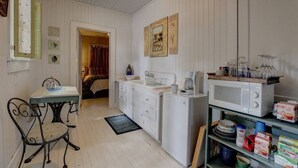 A compact kitchen with white cabinets, a dining table with chairs, a microwave, and a coffee maker. - The Carriage House Downtown Lafayette, LA (Lafayette)