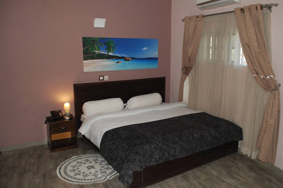 A bedroom with a bed, a nightstand, a wall-mounted air conditioner, and a beach-themed painting.