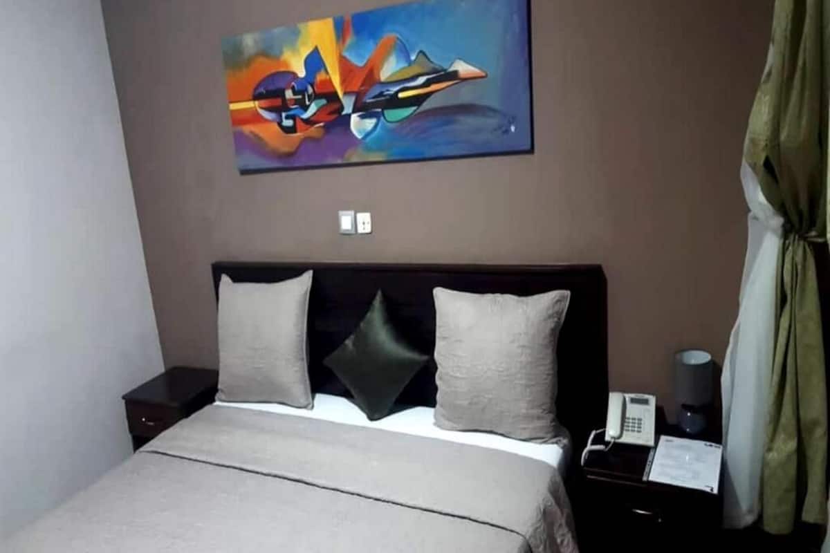 A hotel room with a bed, a nightstand, a telephone, and a painting on the wall.