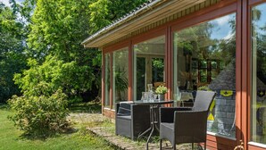 A covered outdoor seating area with wicker furniture, a glass table, and a stone wall with a yellow emblem. - Beautiful home in Grevinge with kitchen (Grevinge)