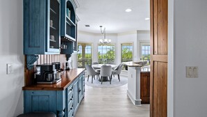 A kitchen with a wooden island, a dining area with a round table and chairs, and large windows with a view of greenery. - Upscale Comfort in Dripping Springs - The Goodnight House - Spacious 4/3 - Views (Dripping Springs)