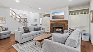 A spacious living room with a fireplace, grey sofas, wooden flooring, and a staircase leading to another level. - Upscale Comfort in Dripping Springs - The Goodnight House - Spacious 4/3 - Views (Dripping Springs)