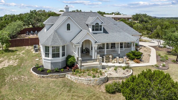 A large, single-story house with a wrap-around porch, a stone foundation, and a landscaped yard. - Upscale Comfort in Dripping Springs - The Goodnight House - Spacious 4/3 - Views (Dripping Springs)