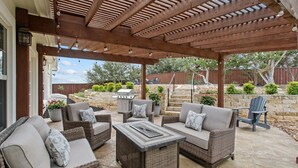 An outdoor patio with wicker furniture, a stone table, and a pergola overhead. - Upscale Comfort in Dripping Springs - The Goodnight House - Spacious 4/3 - Views (Dripping Springs)