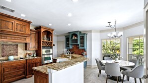A spacious kitchen with wooden cabinets, a central island, and a dining area with a round table and chairs. - Upscale Comfort in Dripping Springs - The Goodnight House - Spacious 4/3 - Views (Dripping Springs)