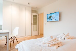 A bedroom with a bed, a desk, a chair, a wardrobe, and a TV on the wall.