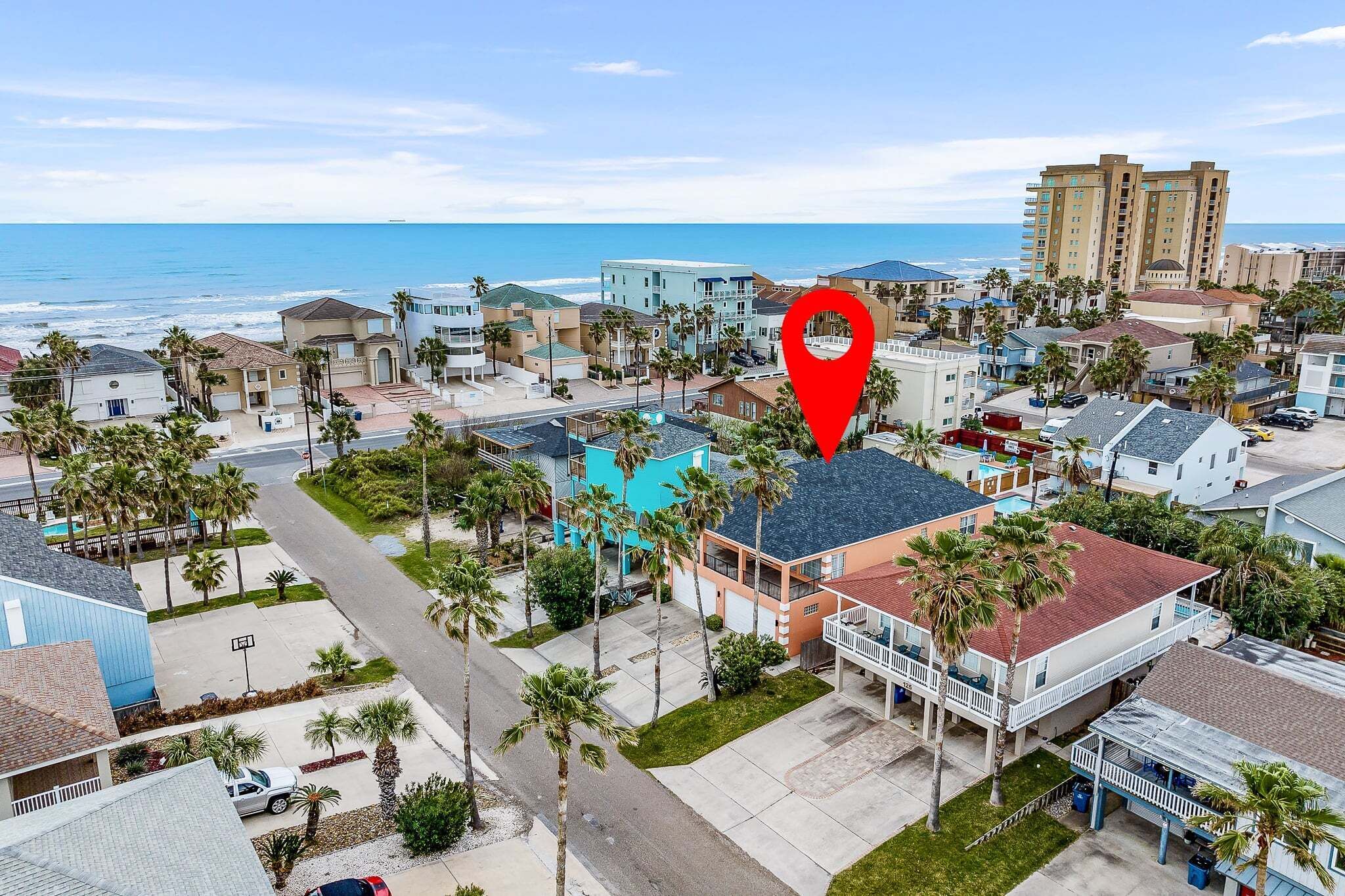 Zona residencial costera con casas unifamiliares y edificios de apartamentos, con palmeras y vista al océano.