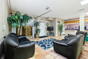 A spacious living area with a black leather sofa set, a large potted plant, and a tiled floor.